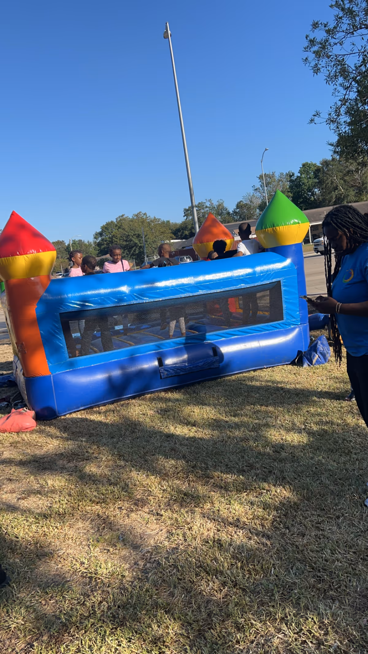 Children play on a blue inflatable bounce house outdoors, with adults nearby.