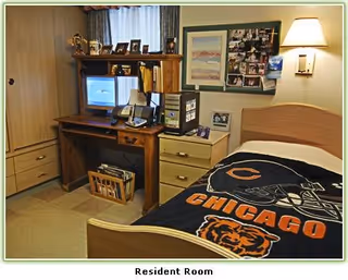 Resident room featuring a bed, desk computer setup, TV, photos, and Chicago Bears blanket.