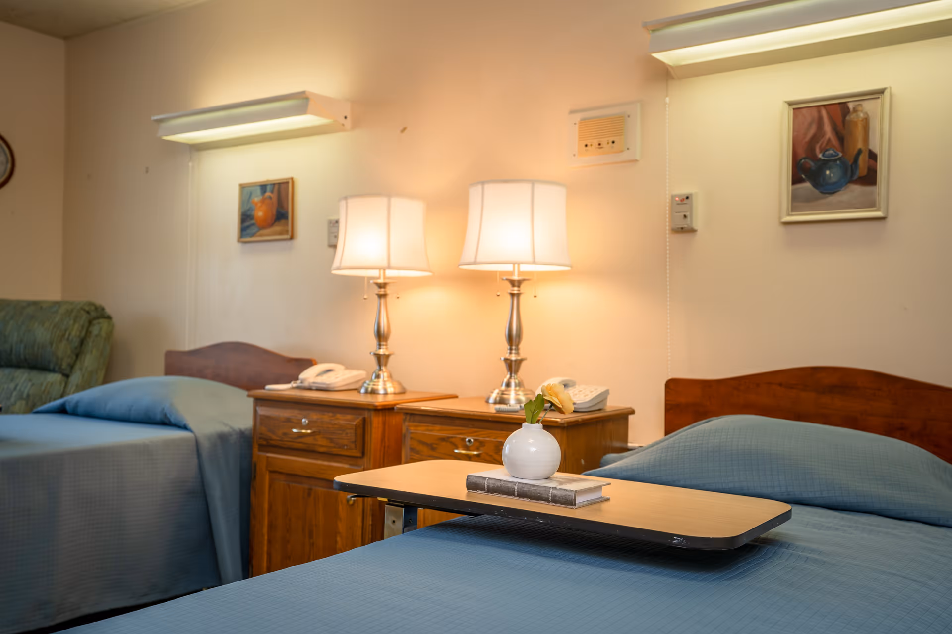Two beds with blue bedding, matching nightstands, lamps, and a small tray between them.