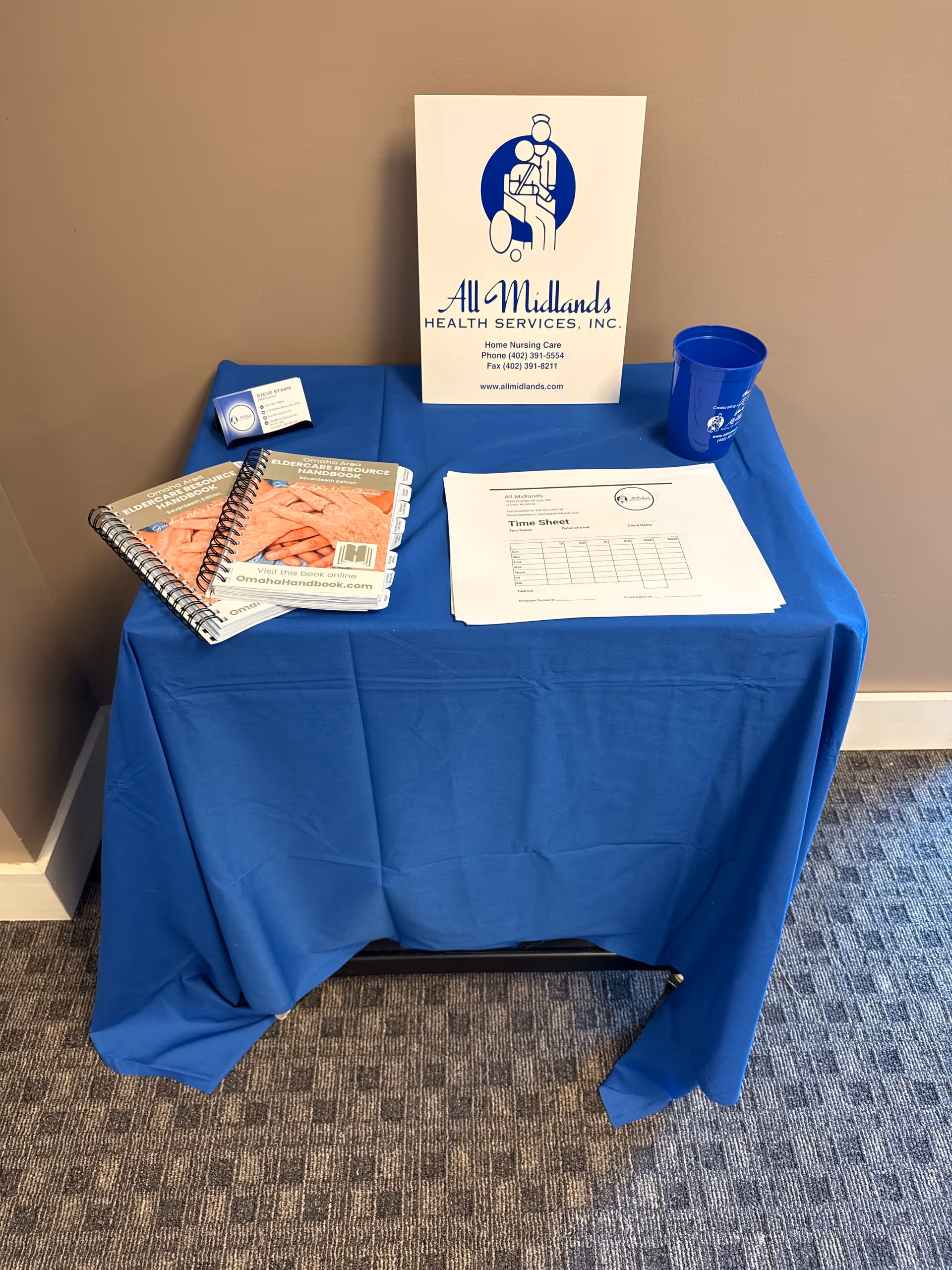 Blue-draped table with All Midlands Health Services sign and brochures in a hallway.