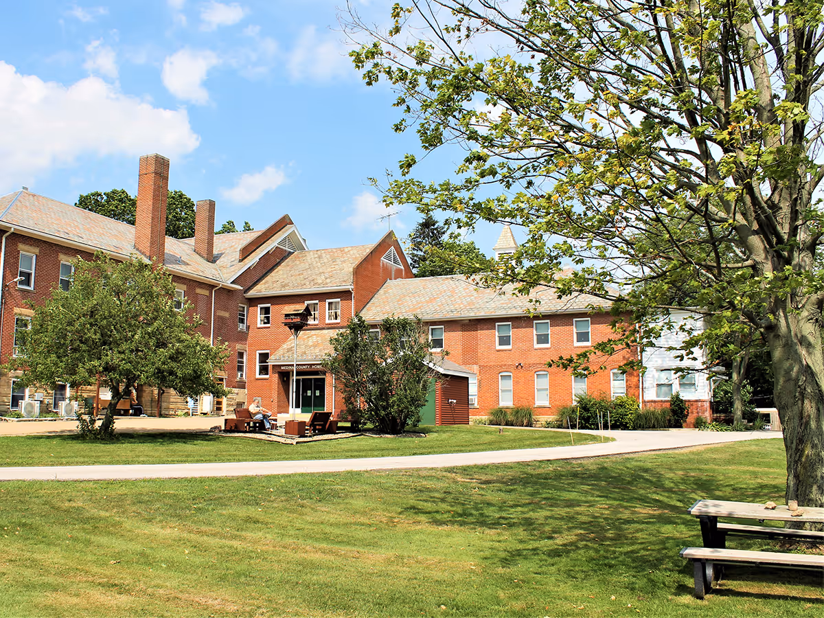 Red brick senior living campus with lawns, trees, and a curved walkway.
