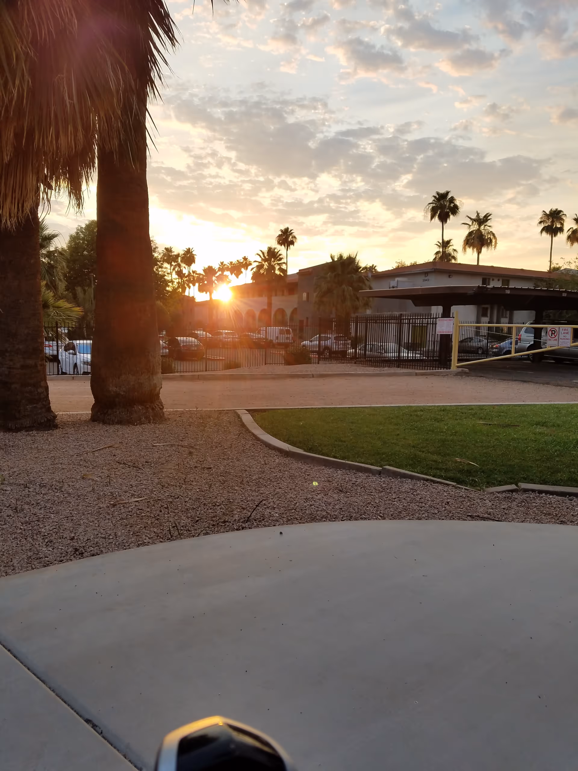 Sunset over a gated assisted living facility courtyard with palm trees and parked cars.
