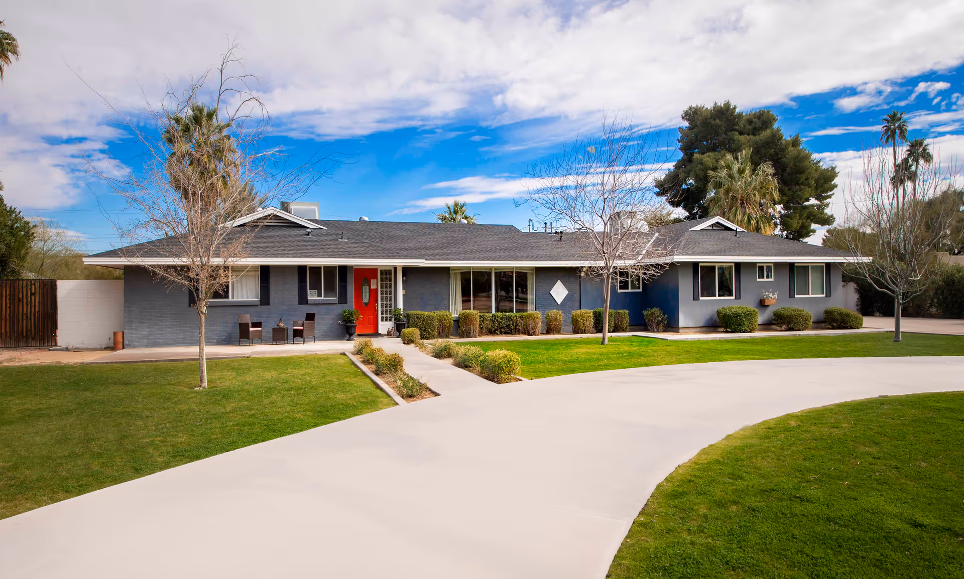 Single-story blue building with red door, manicured lawn, and curved concrete driveway.