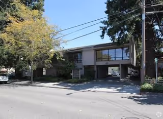 Two-story building with large windows and a driveway, surrounded by trees and power lines.