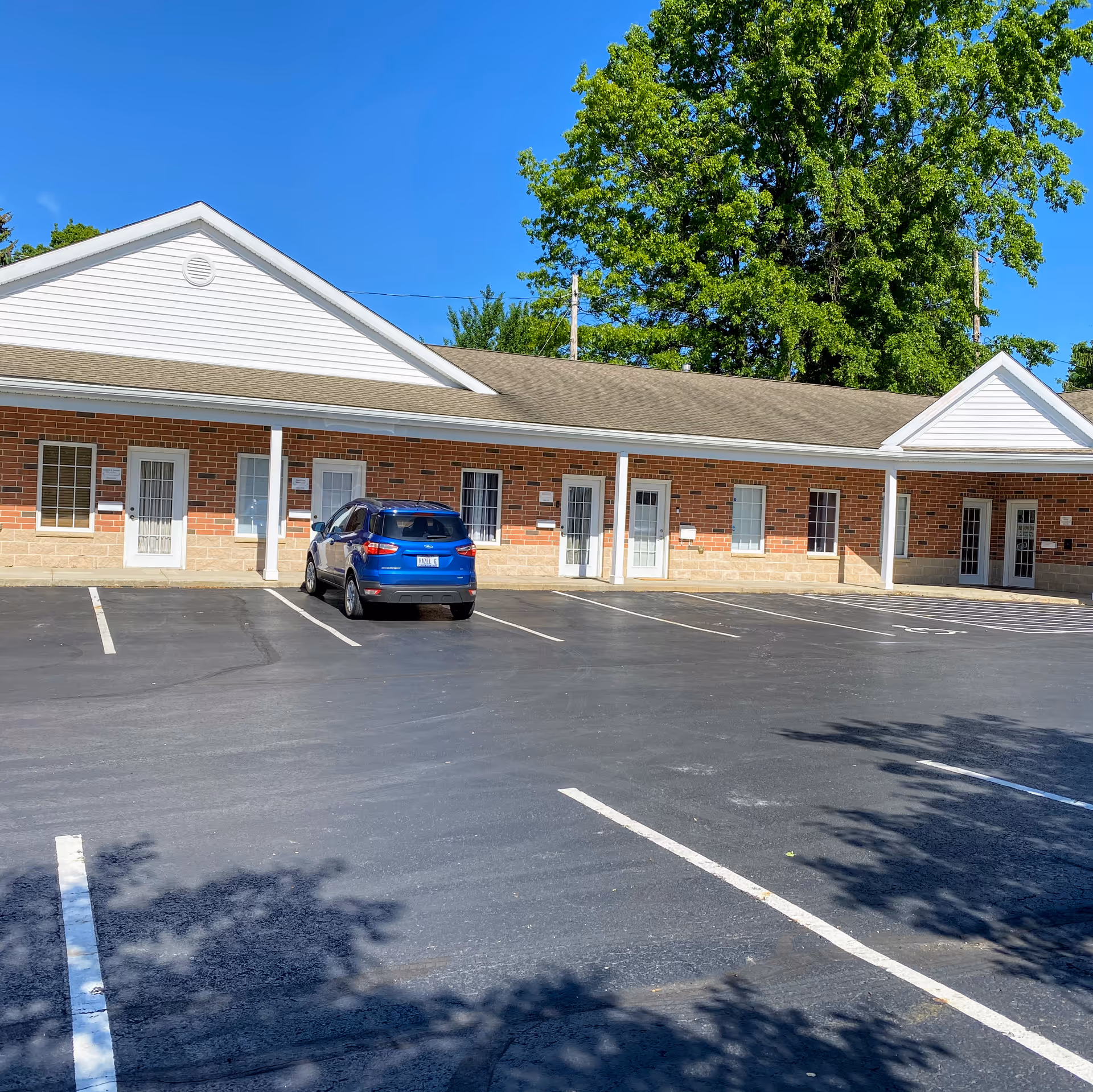 Exterior of a single-story brick building with white doors and a blue car in parking lot.