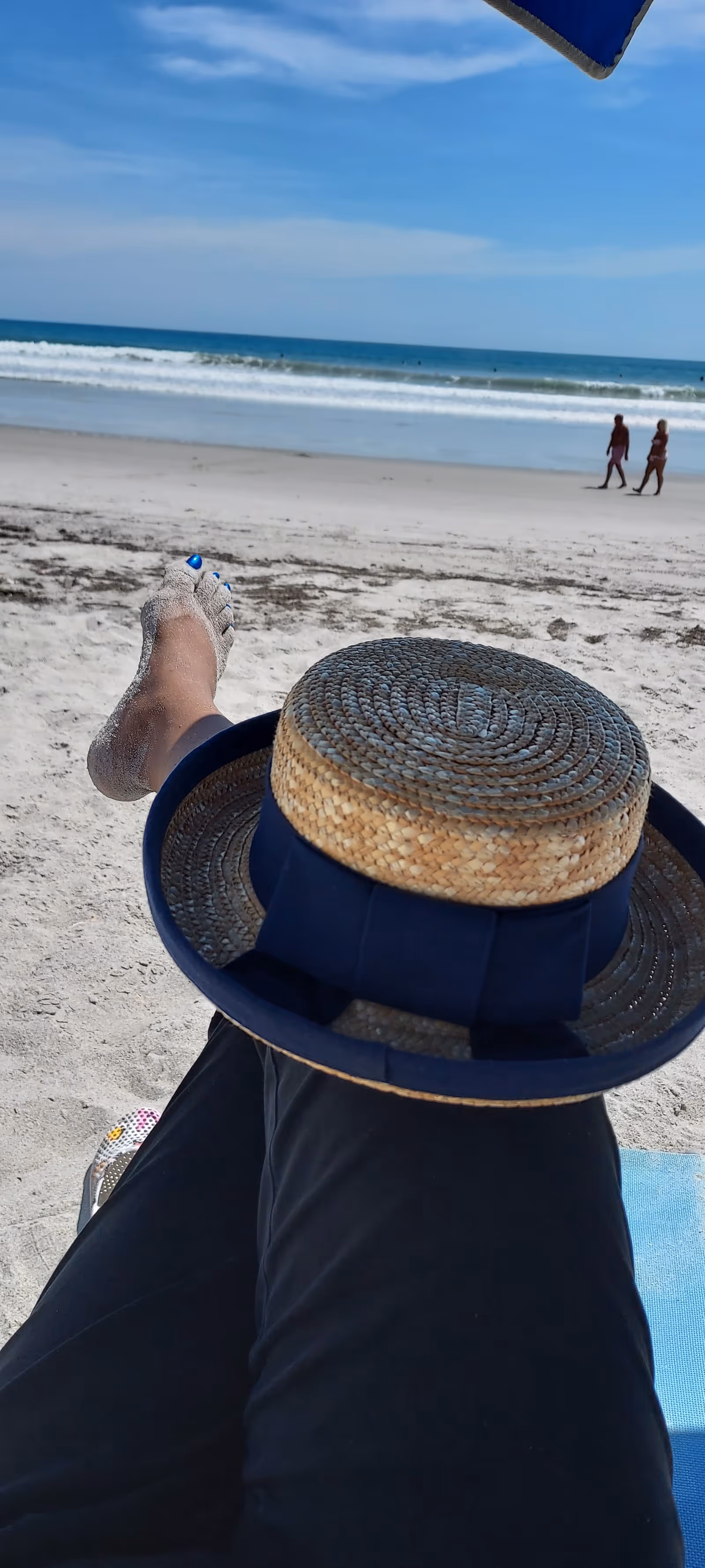 Person lounging on a beach chair with hat, ocean waves in the distance.