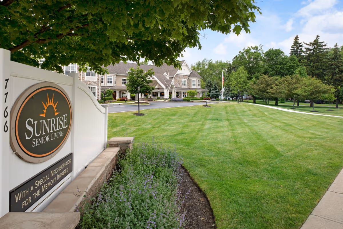 Front lawn and entrance of the Sunrise Senior Living building with a large sign in the foreground.