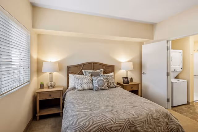Cozy bedroom with a made bed, twin nightstands, lamps, and a nearby laundry area