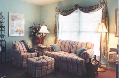 Cozy living room with striped sofa, matching chair, ottoman, lamps, and draped windows.