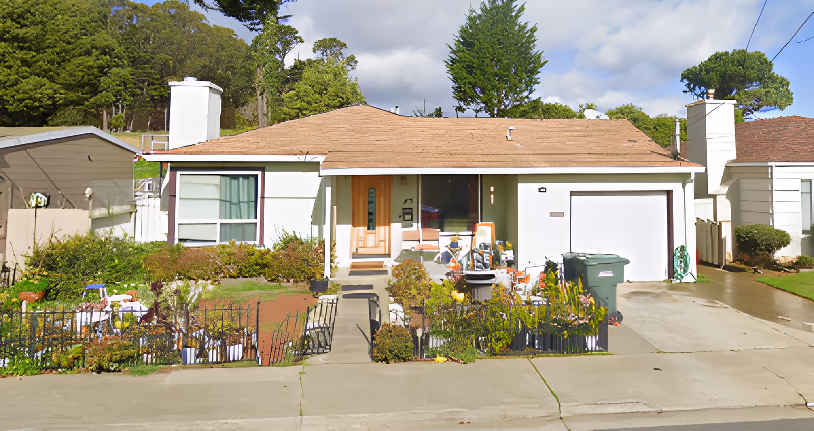 Front exterior of a single-story suburban house with a garage, driveway, small fenced garden, and porch.