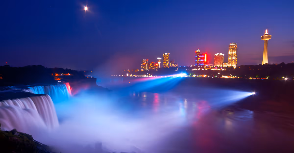 Nighttime view of Niagara Falls with an illuminated distant city skyline.