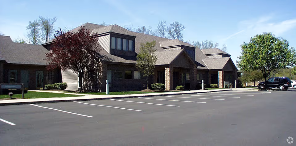 A single-story senior living facility with a paved parking lot and trees in front.