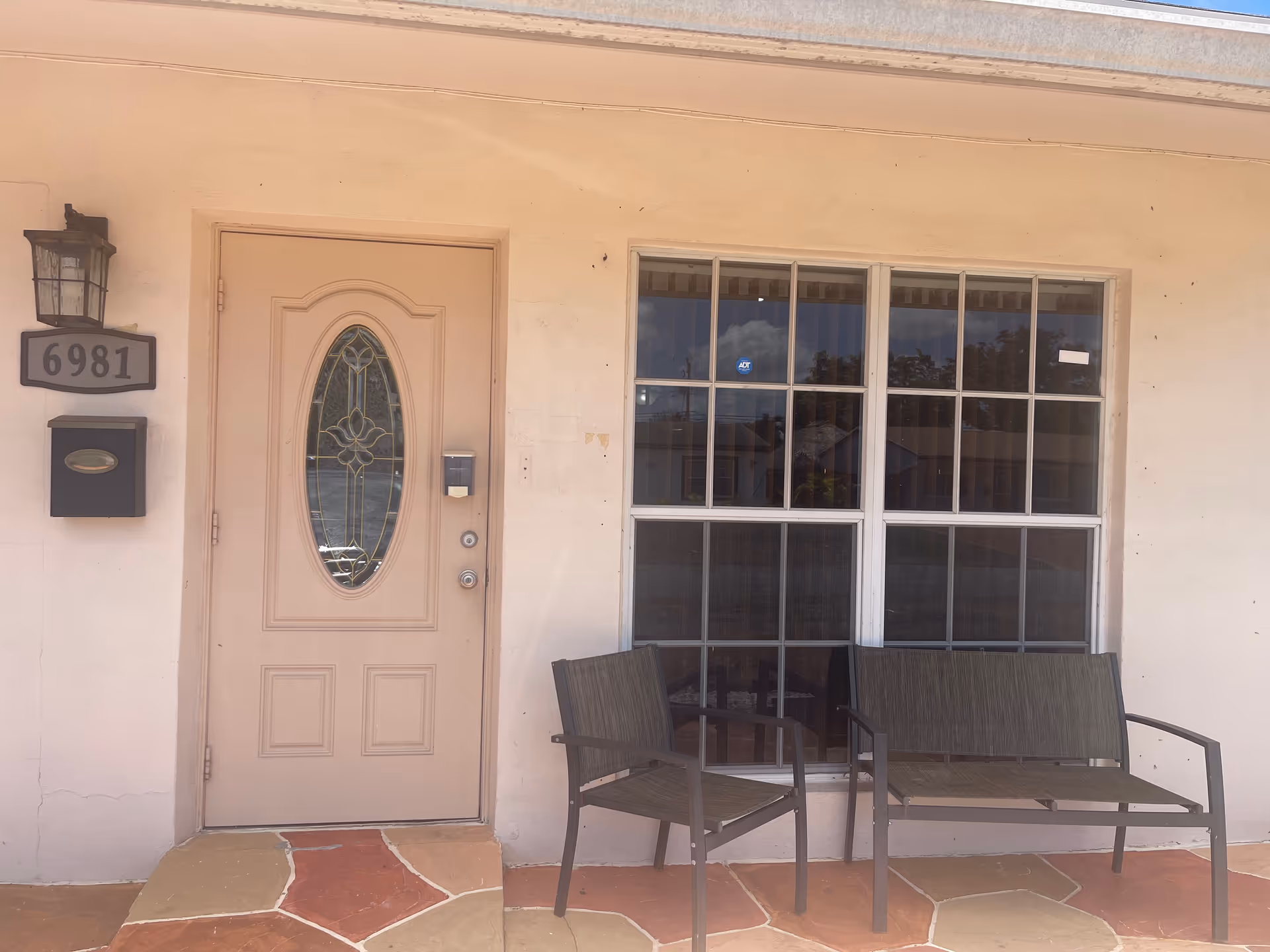 Front exterior of a home-style senior facility with door, large window, and outdoor seating.