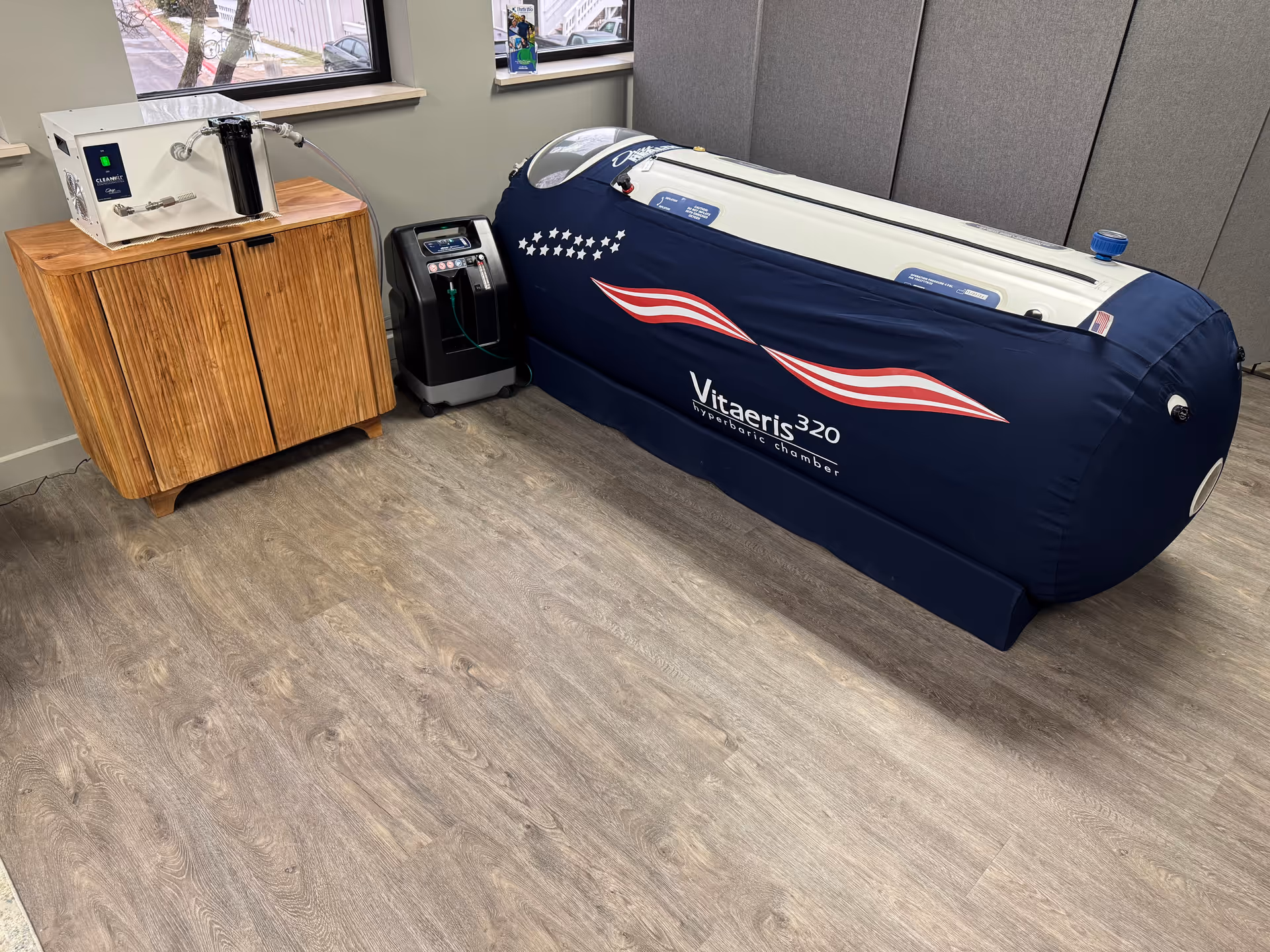 A blue Vitaeris 320 therapy chamber sits in an interior room beside a wooden cabinet.