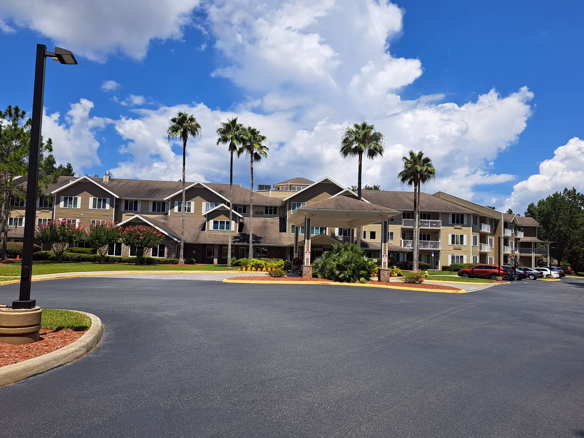 Exterior view of Marion Woods Sky Active Living building with circular driveway and palm trees.
