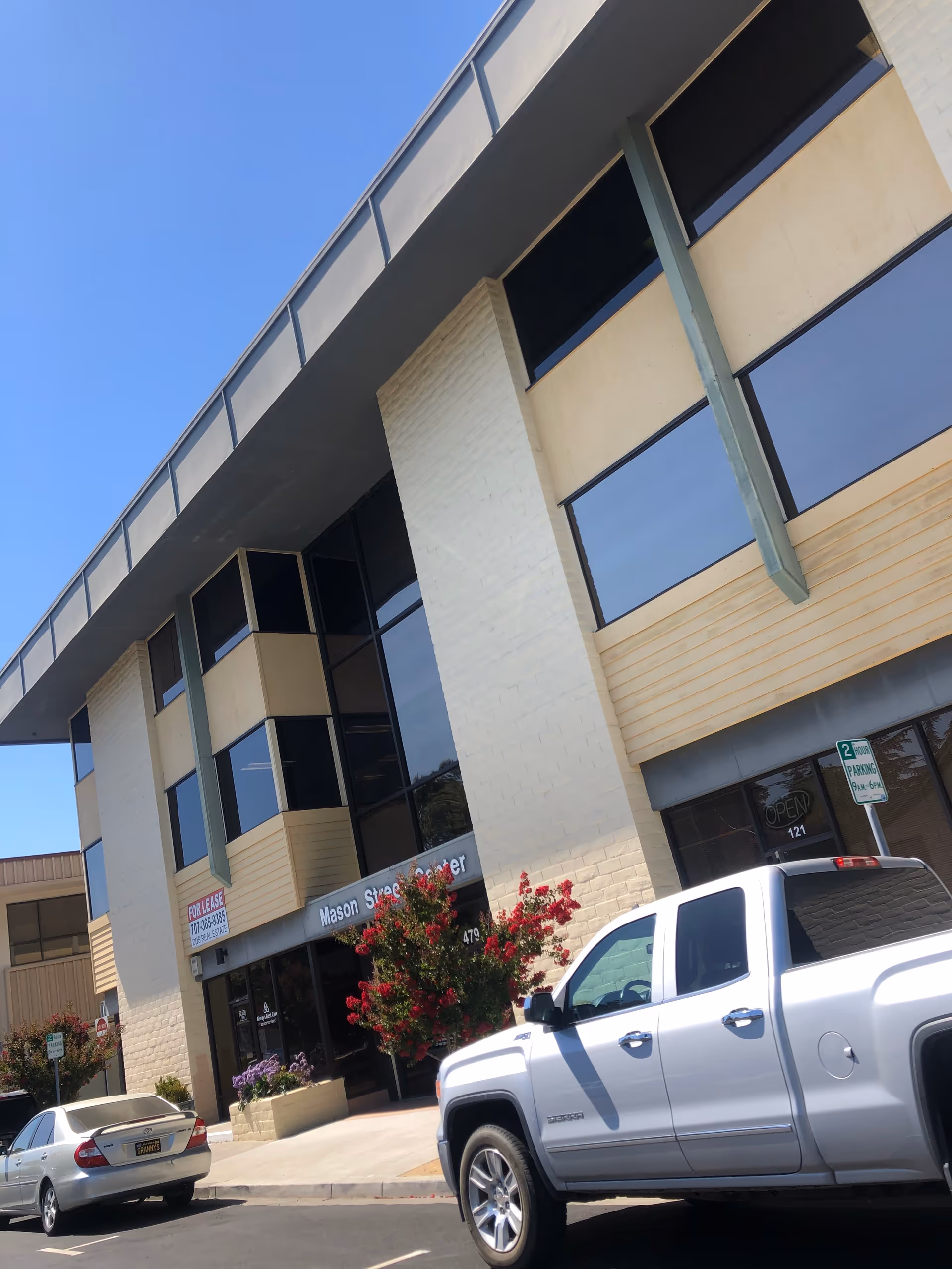 Modern building exterior with large windows and parked cars along the curb.