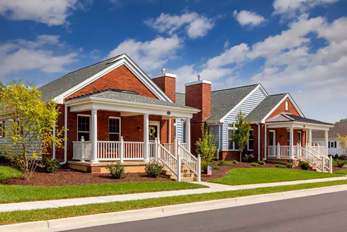 Row of brick, cottage-style senior living buildings with white porches along a street.