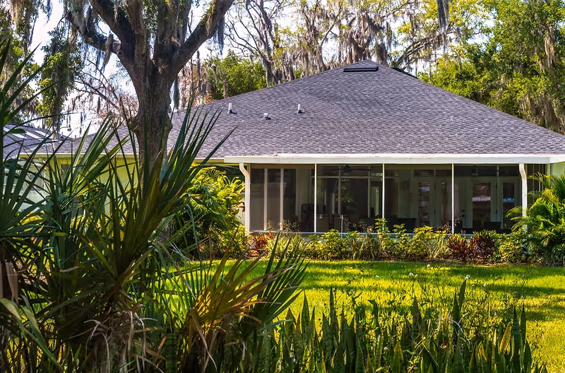 Single-story assisted living facility with a grassy lawn, shrubs, and a screened front porch.