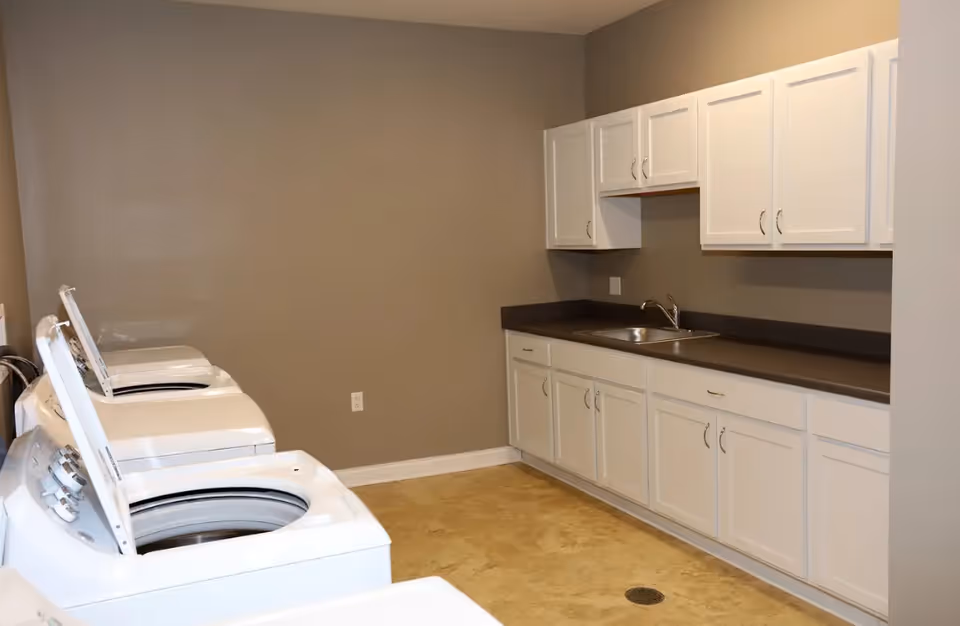 Laundry room with white cabinets, counters, sink, and washers along beige wall.