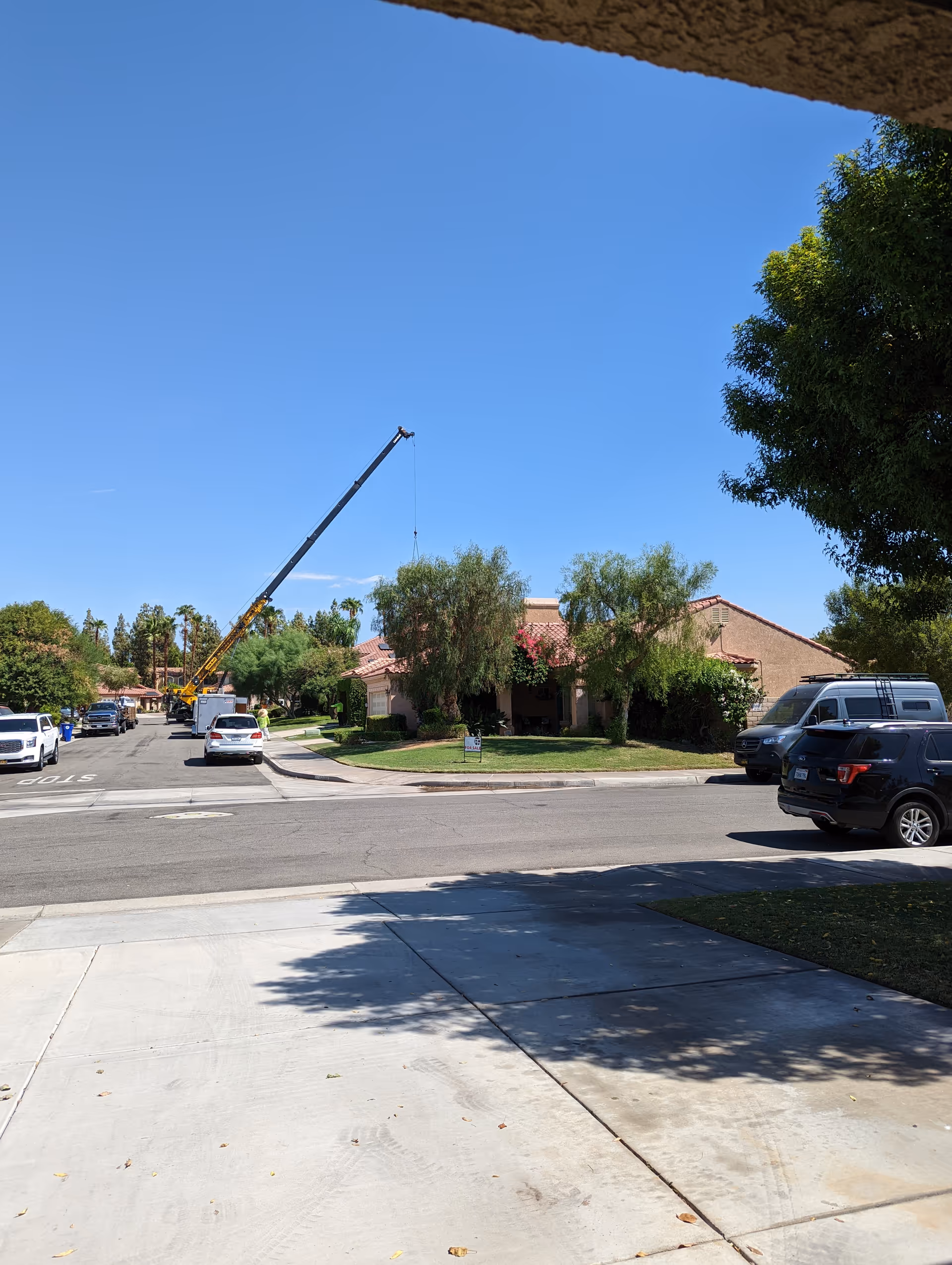 Outdoor street view of a single-story senior living center with a crane, cars, and trees.