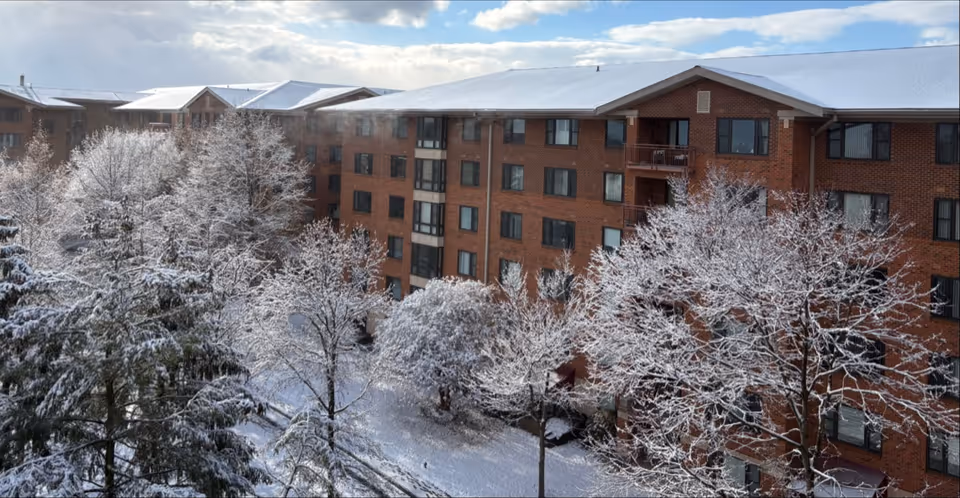 Snow-covered trees surround a brick senior living building seen from above.