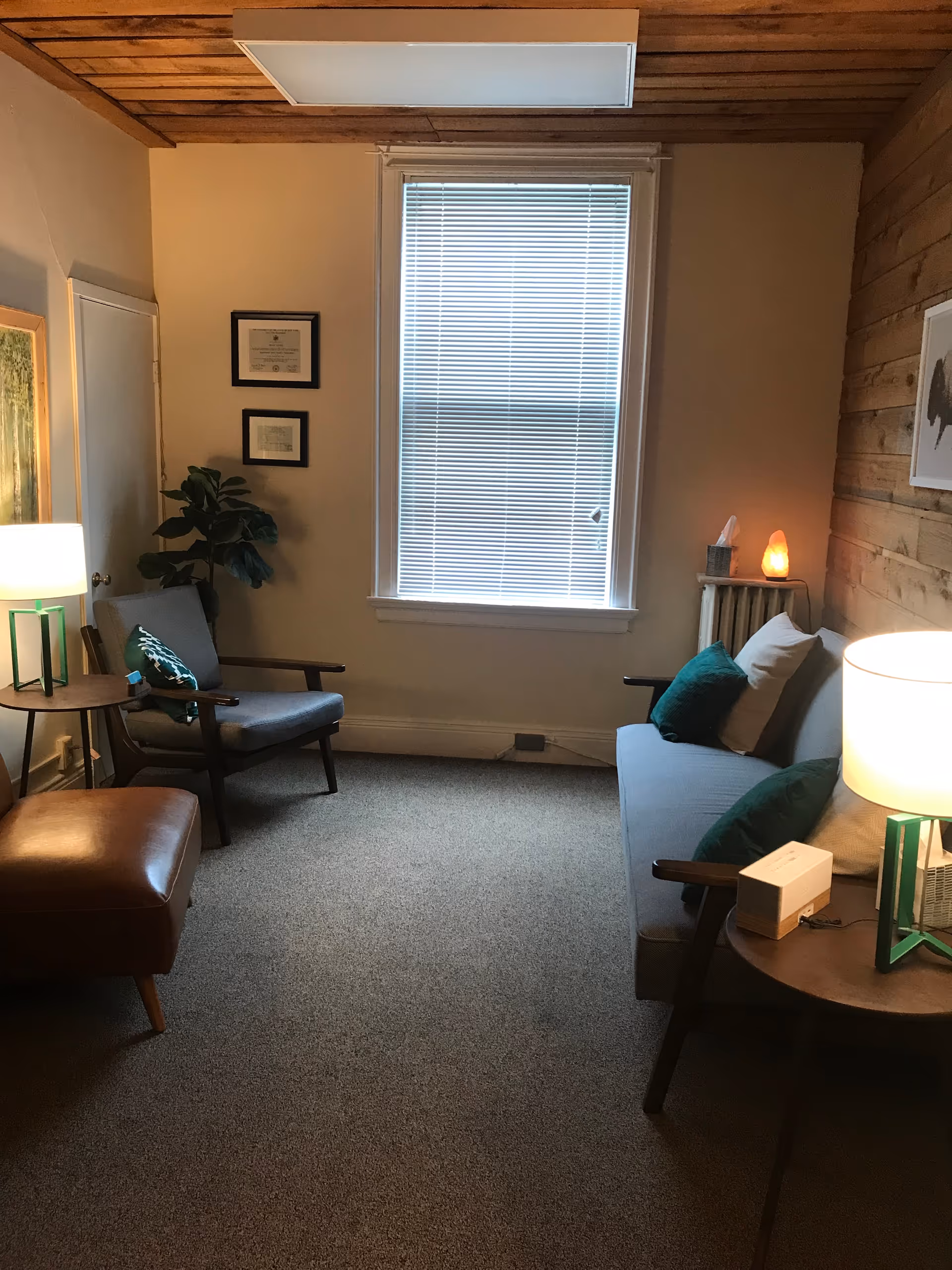 Cozy living room in a senior facility with sofa, chairs, lamps, and window blinds.