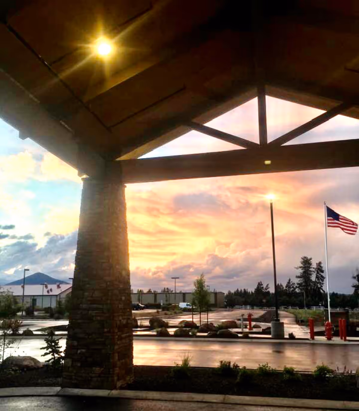 Covered entrance with a stone pillar, flagpole, and sunset-lit parking lot exterior.
