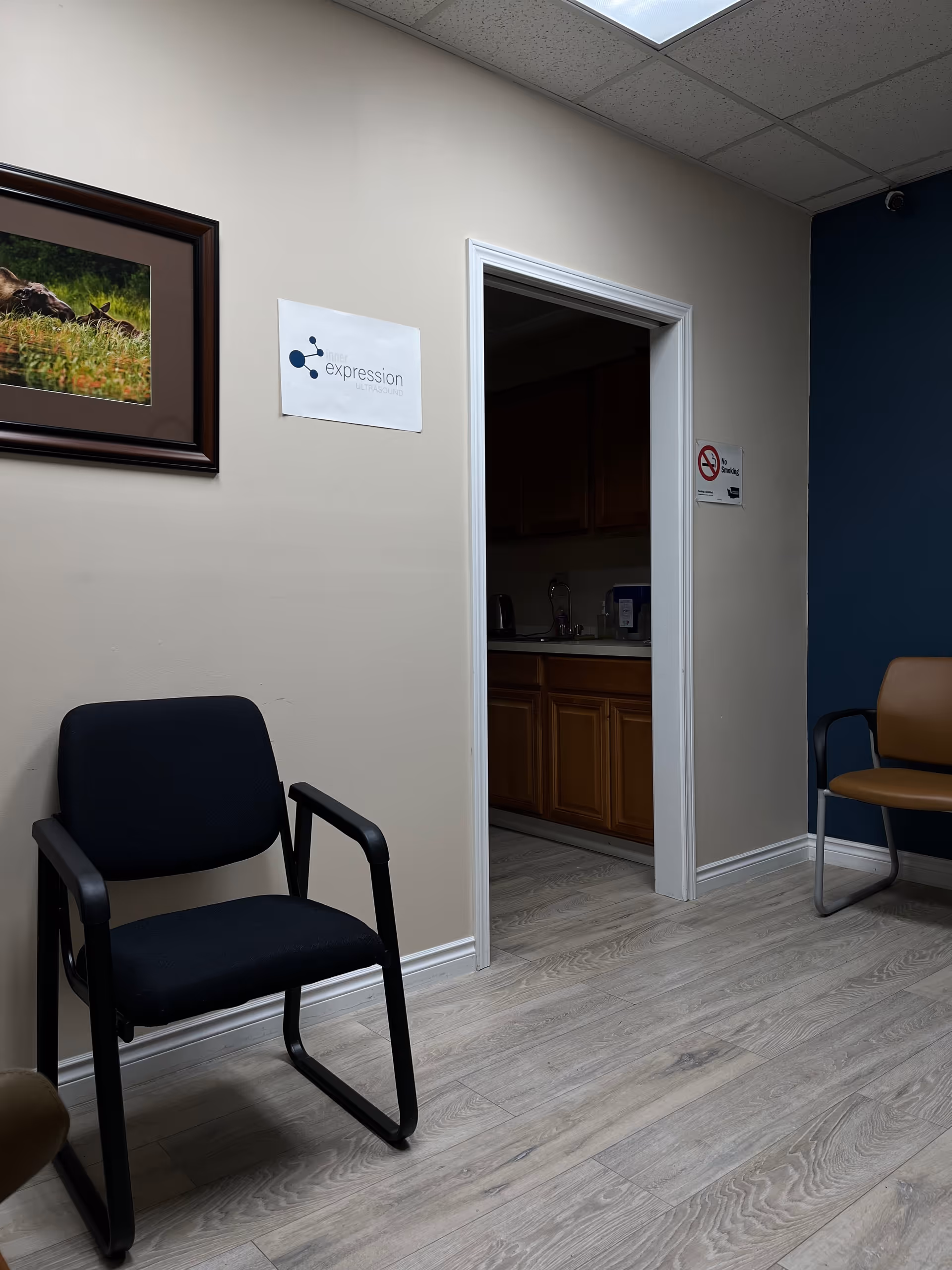 Interior waiting area with blue chair, framed photo, and doorway to kitchenette.
