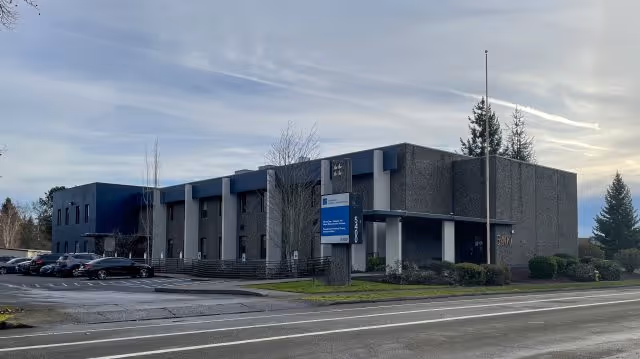 Modern gray and blue building exterior with a parking lot and front entrance.