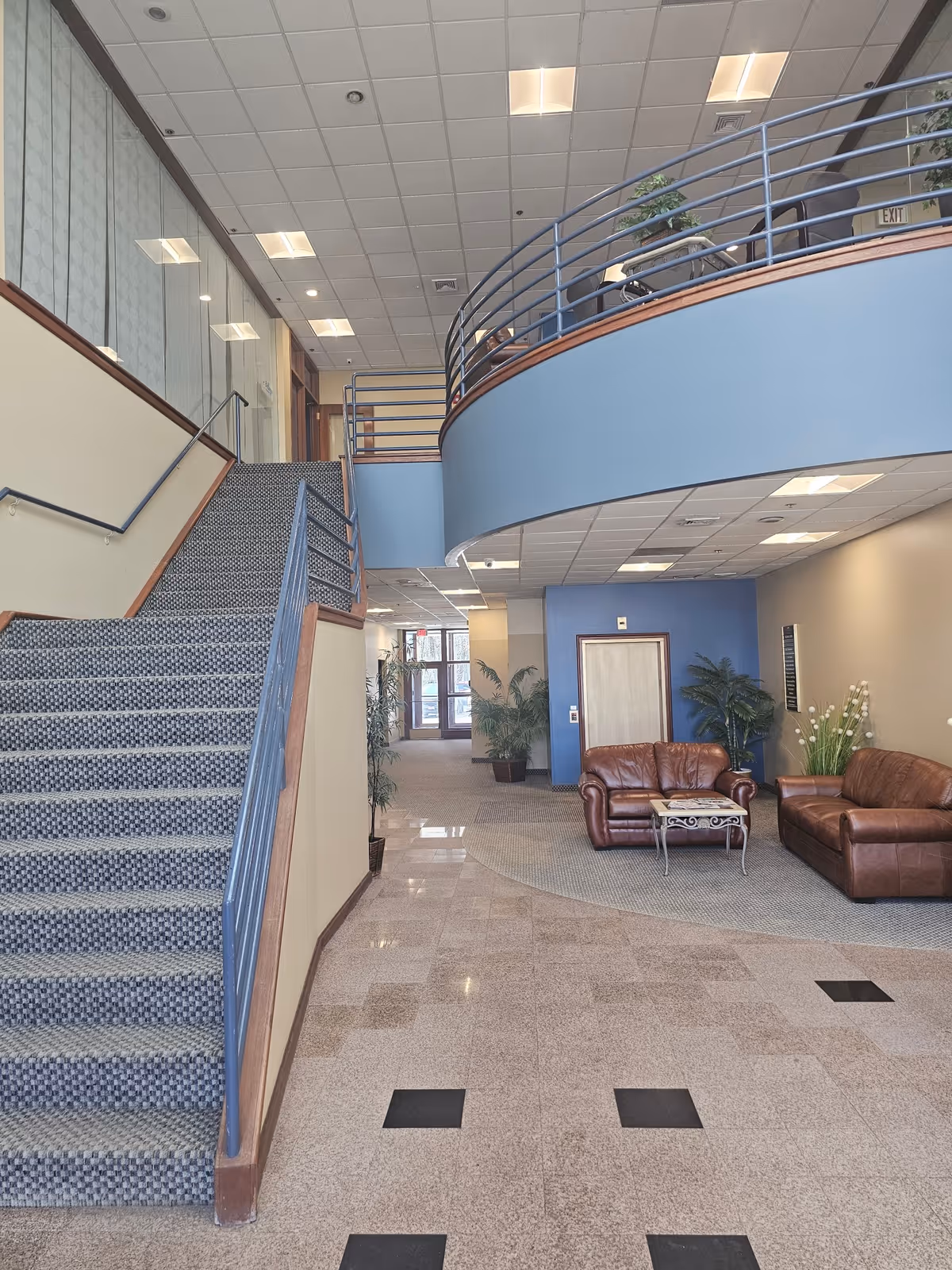 Spacious interior lobby with curved balcony, staircase, and leather seating.