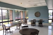 Sunlit dining area with tables and wooden chairs inside a senior care facility.