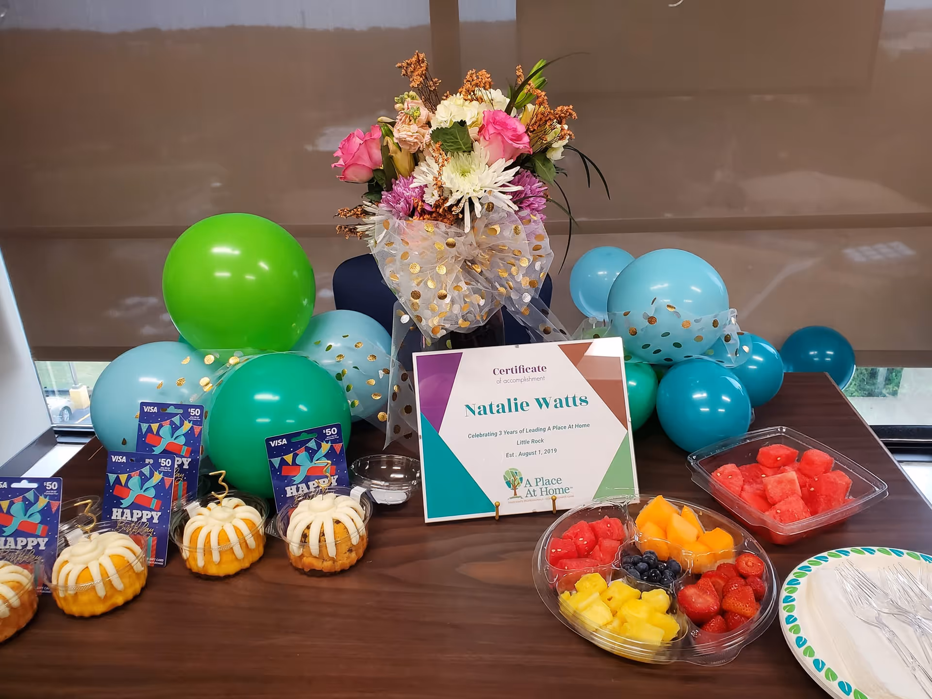 Table celebration setup with bouquet, balloons, cupcakes, and a fruit tray.
