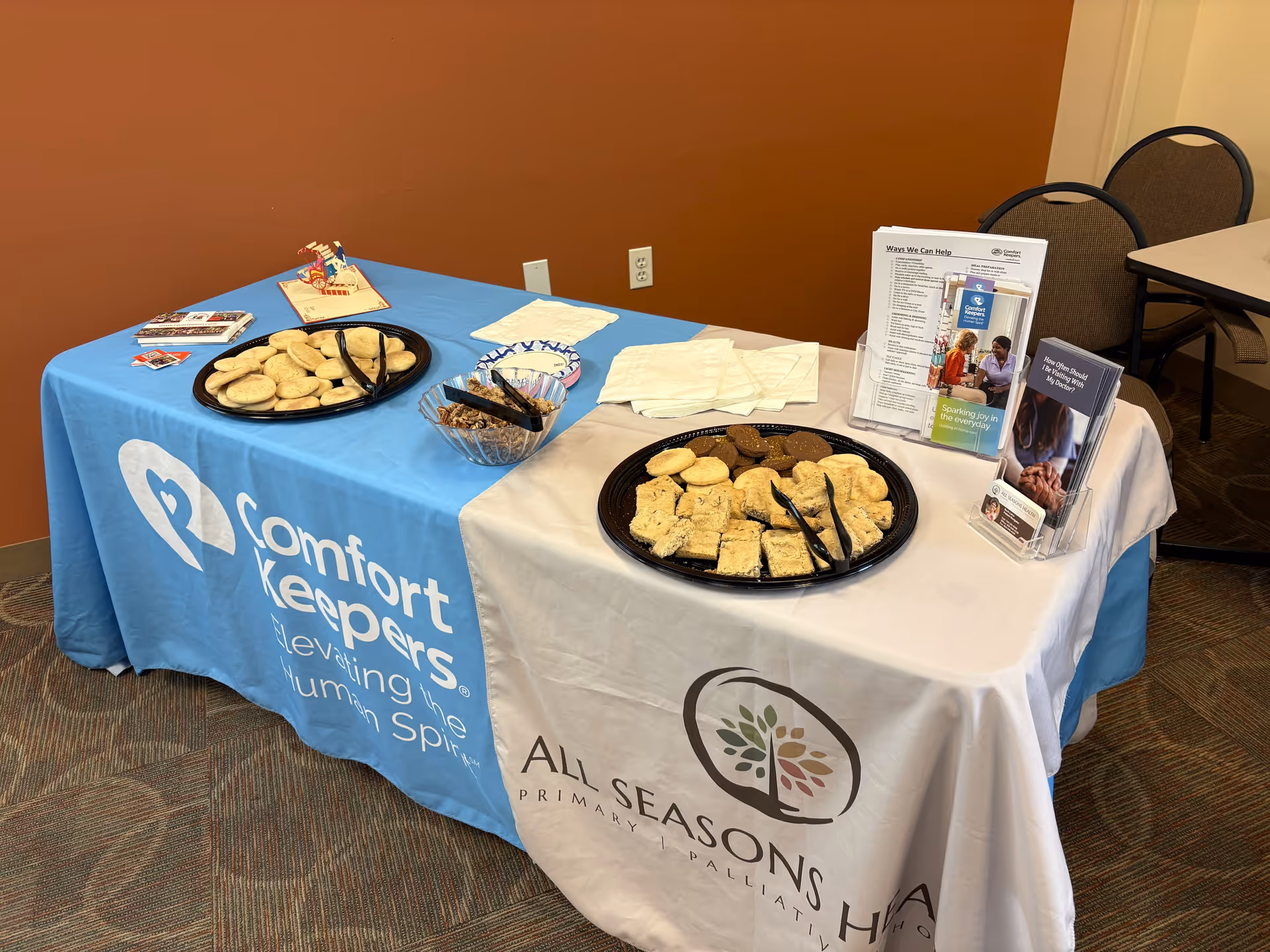 Promotional display table with cookies and brochures for Comfort Keepers in a meeting room.