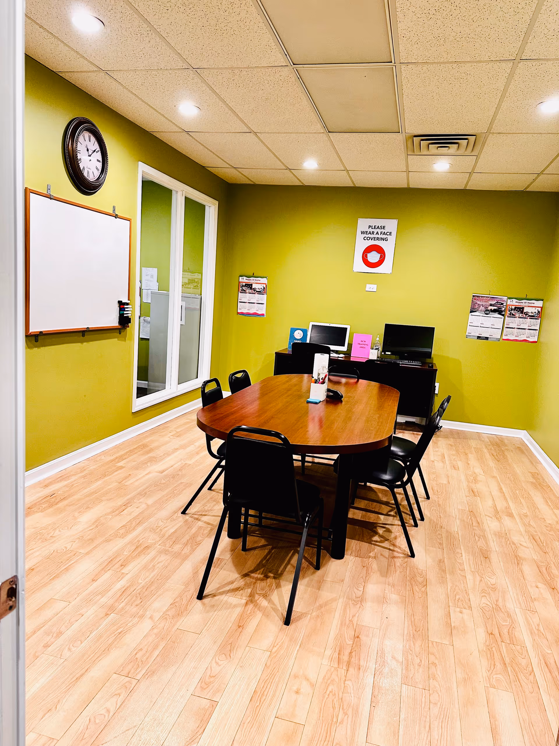 Green-walled indoor dining room with a wooden table, chairs, whiteboard, and computers.