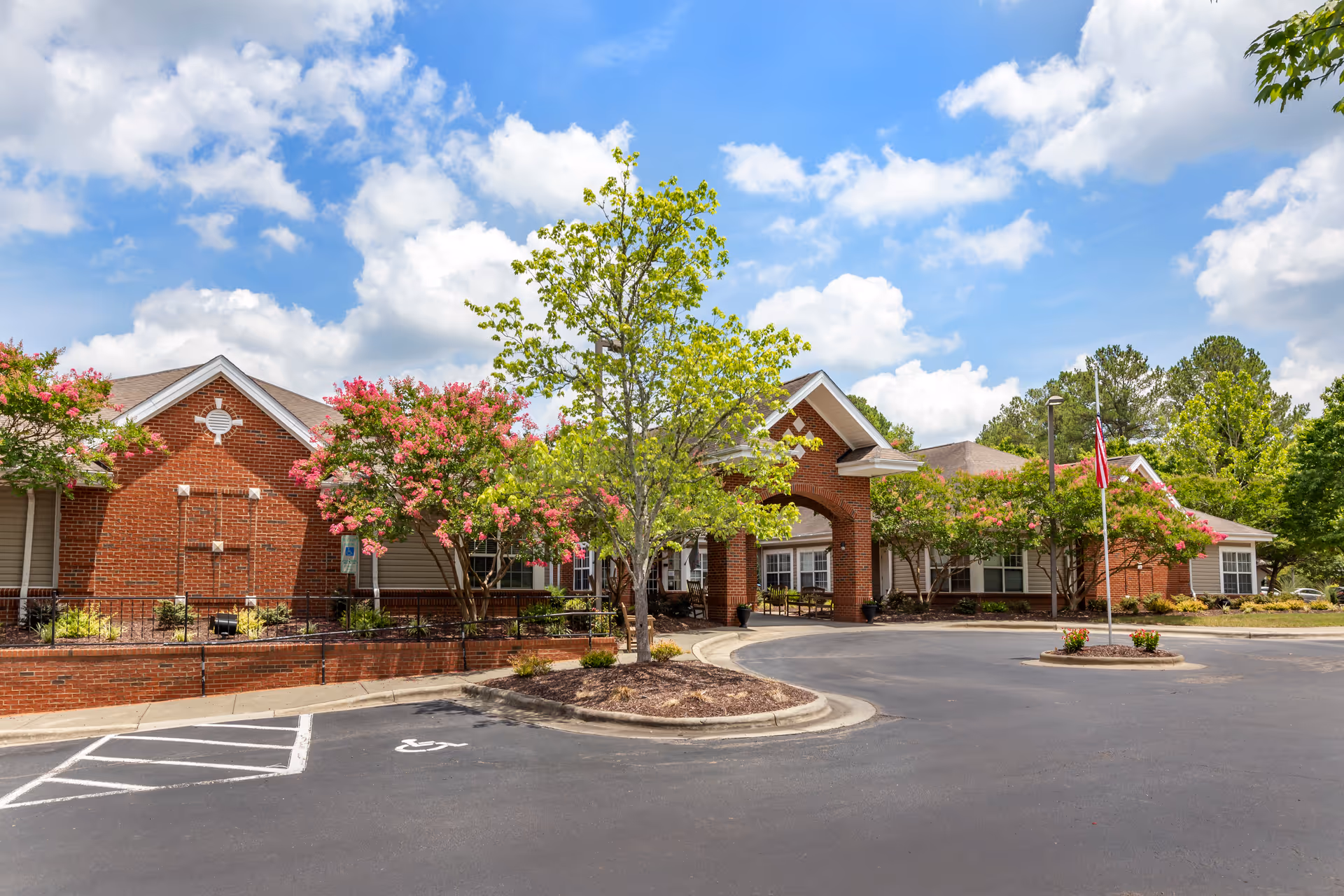 Exterior view of a brick senior living facility with arch entrance, trees, and a circular driveway.