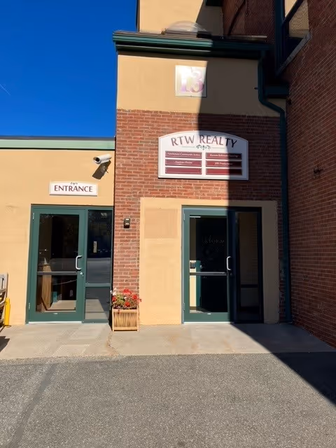 Exterior view of a brick building entrance with glass doors and signage.