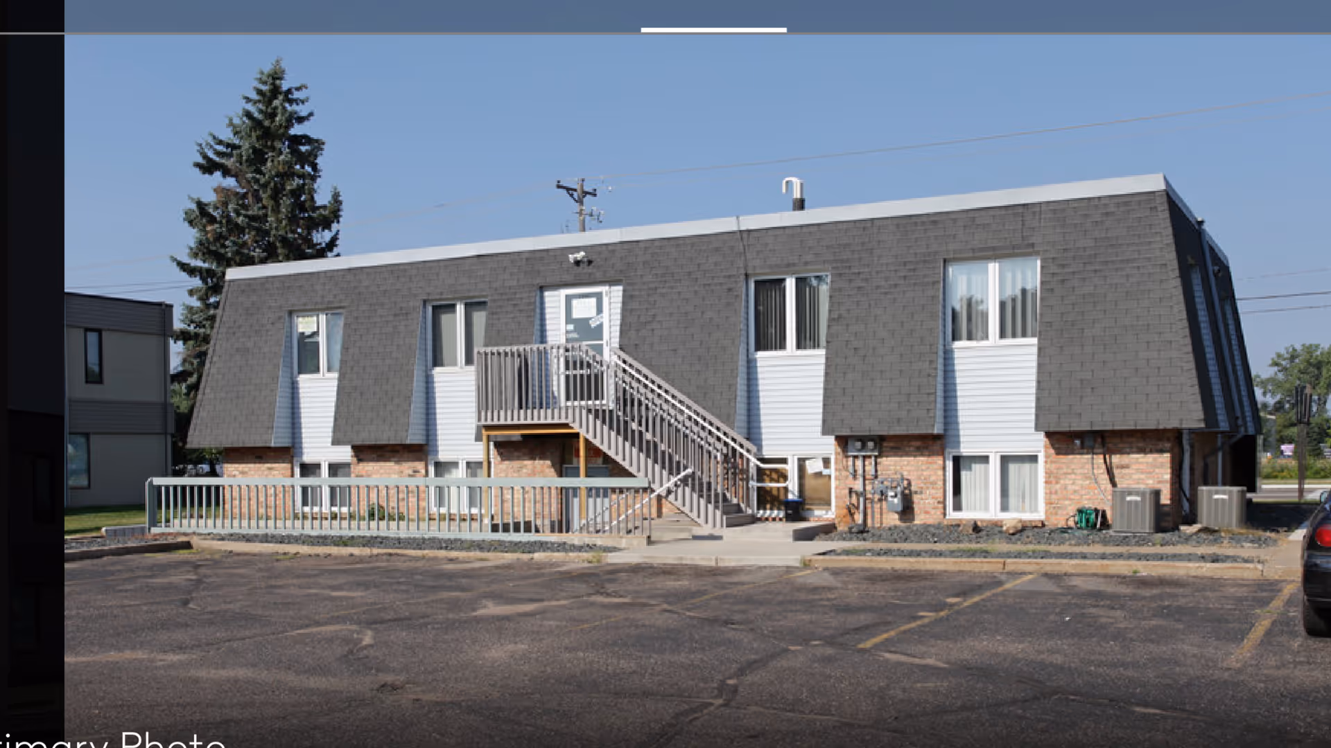 Exterior view of a two-story senior care building with stairs and a parking lot.