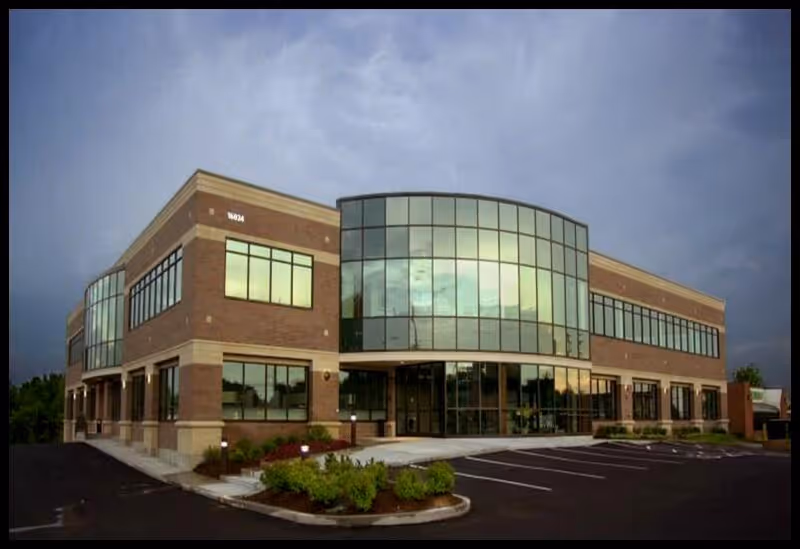 Two-story brick building with curved glass entrance and surrounding parking.