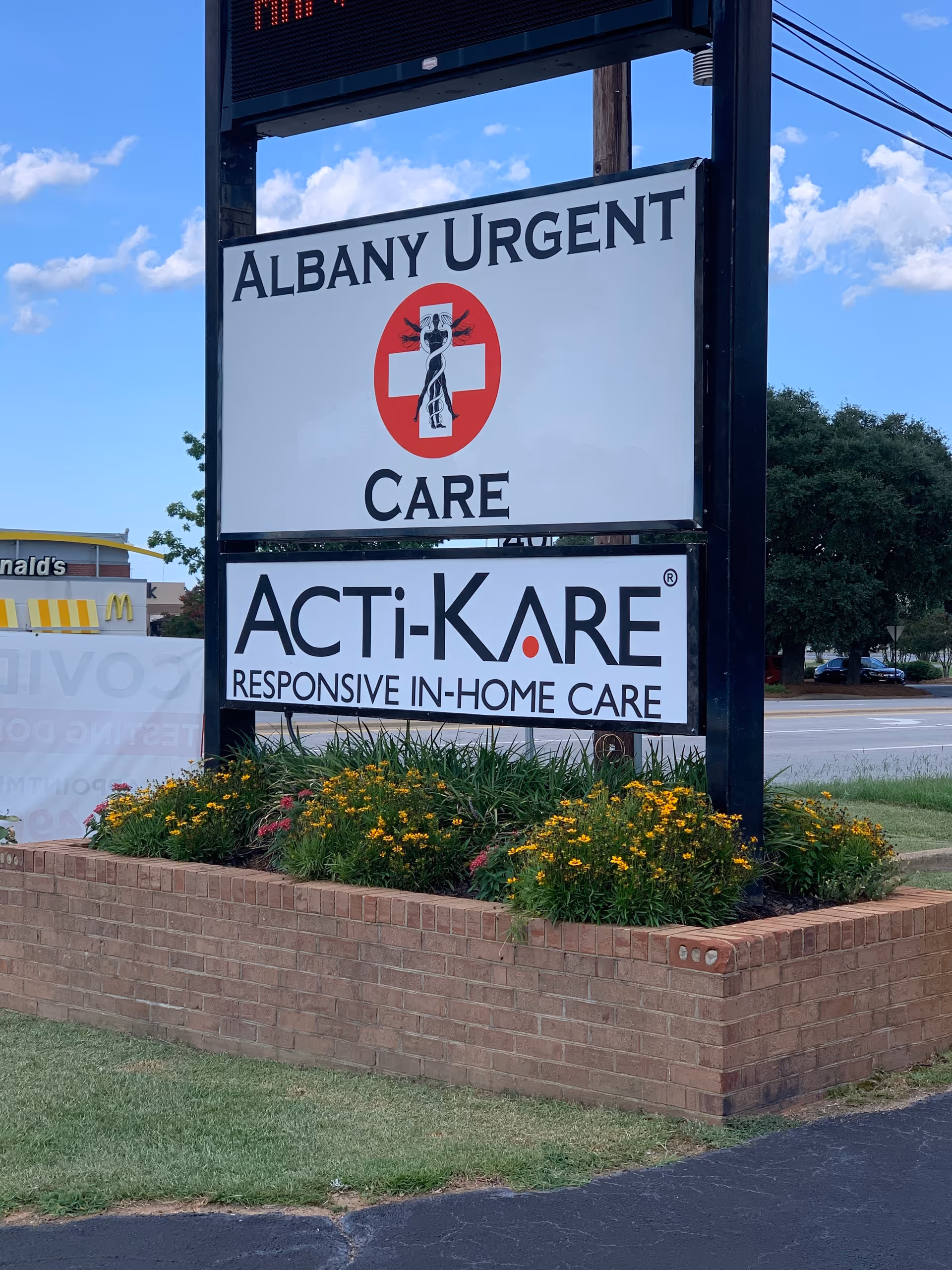 Exterior sign display for Albany Urgent Care and Acti-Kare Senior & Home Care with flowers.