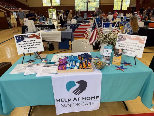 Table at a senior care expo featuring Help at Home Senior Care and American flags.