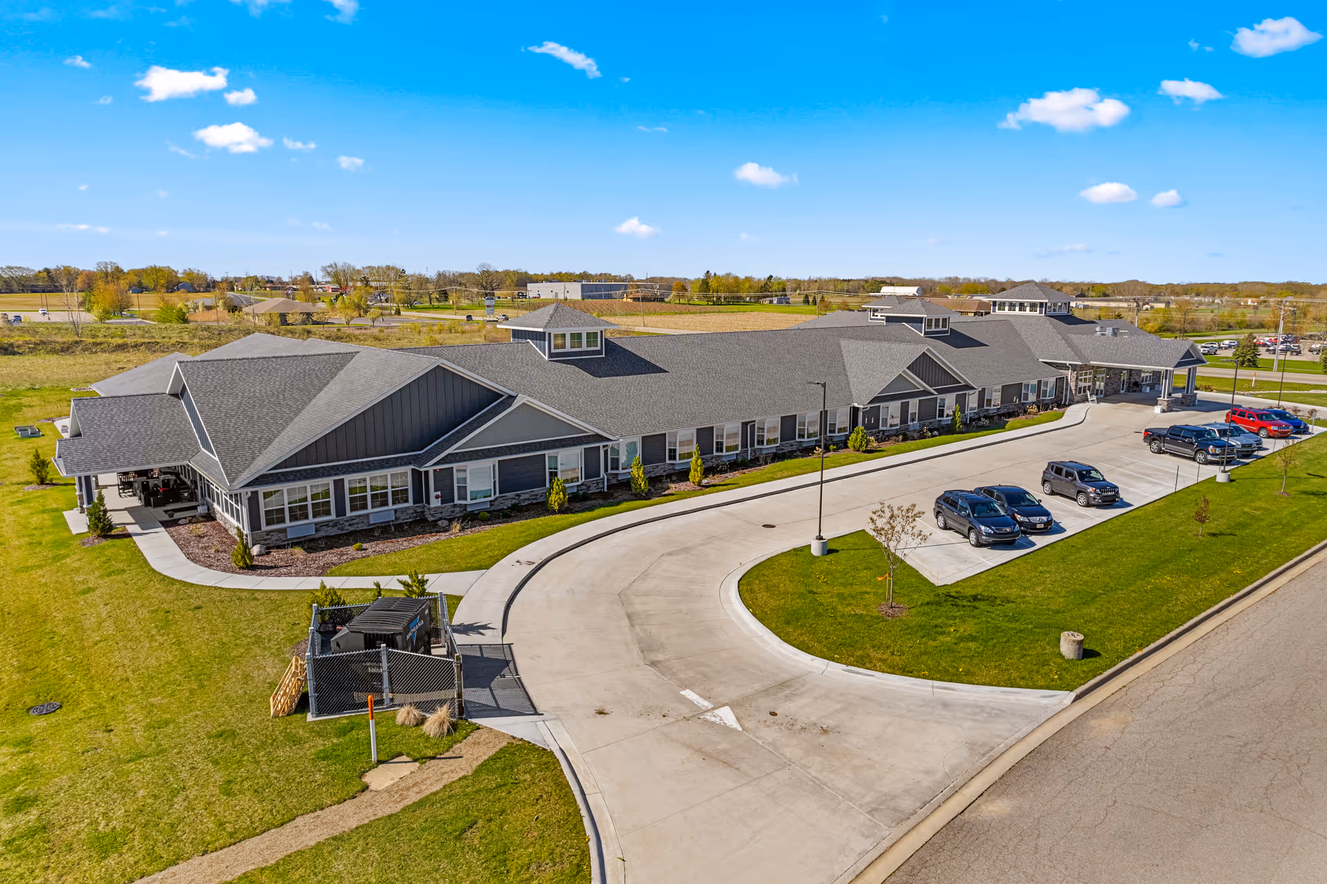 A sprawling, single-story senior living campus with a curved driveway and parked cars.