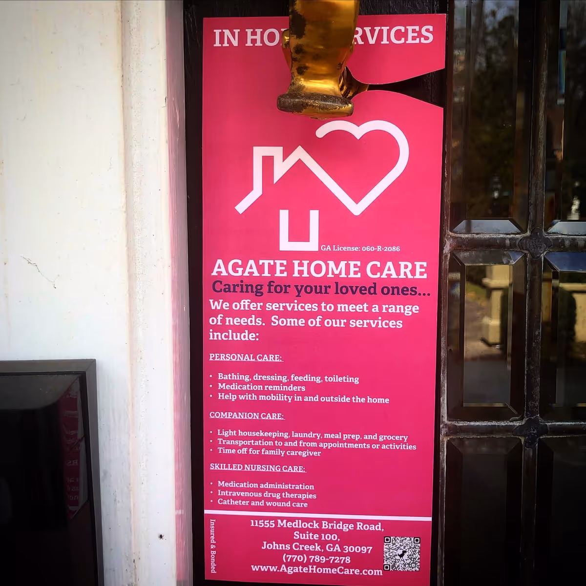 Bright pink Agate Home Care sign posted on a glass door at building entrance.