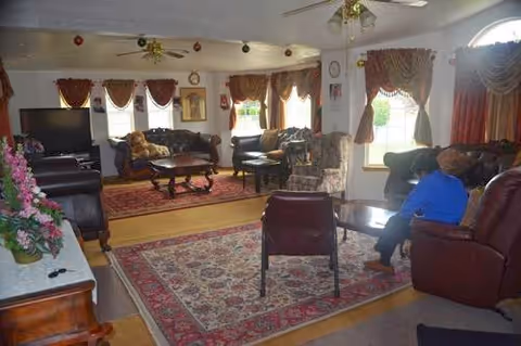 A cozy senior living common room with couches, chairs, rugs, and a TV.