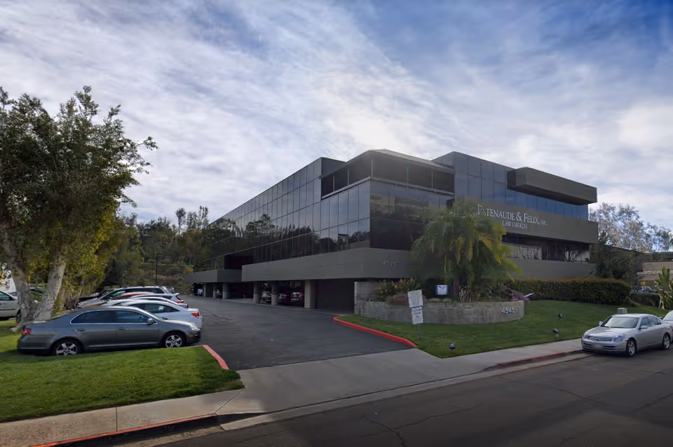 Modern glass office building with dark panels, palm trees, and a multi-vehicle parking area.