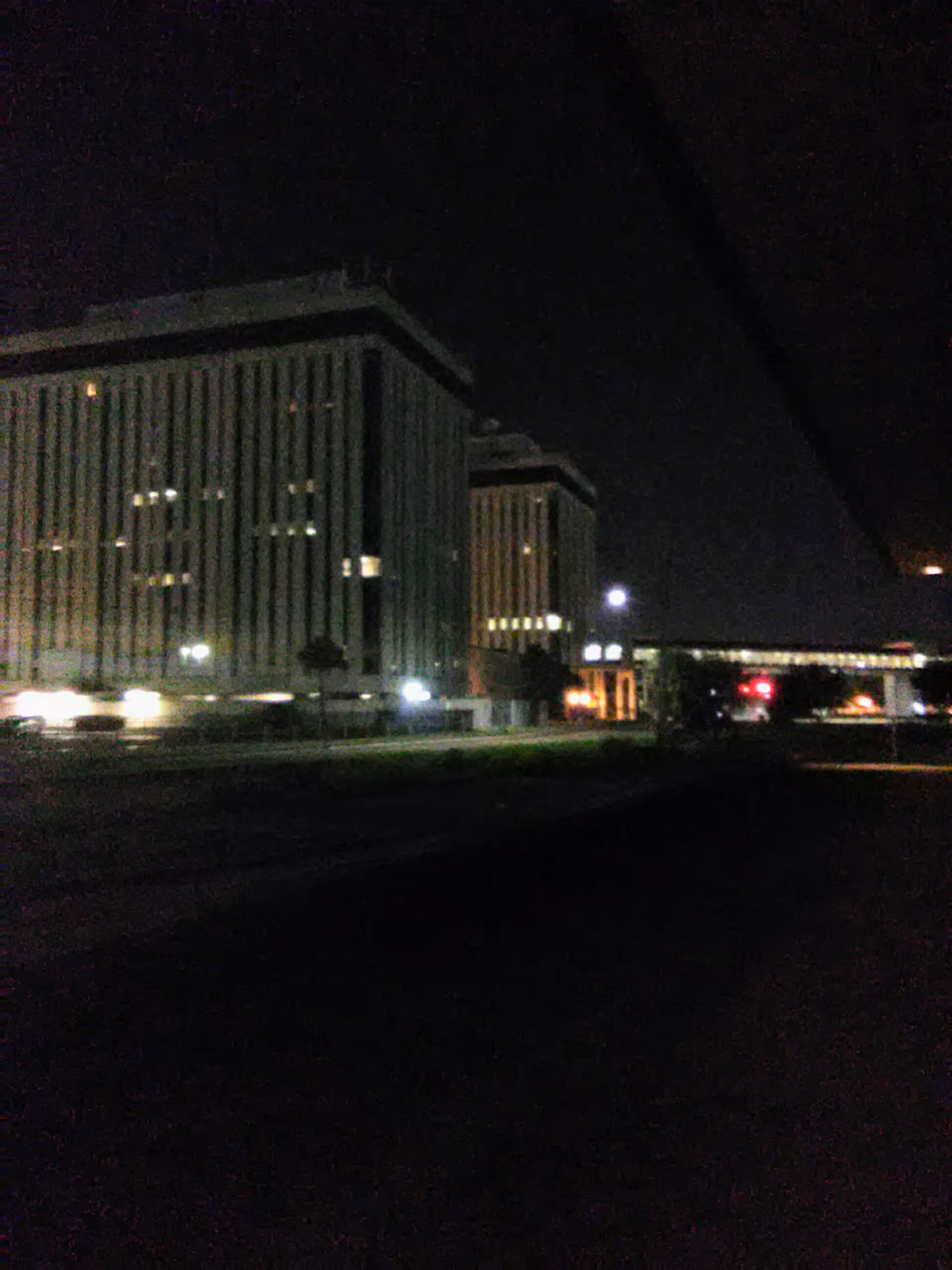 Night exterior of a modern UF Health facility with illuminated windows and a walkway.