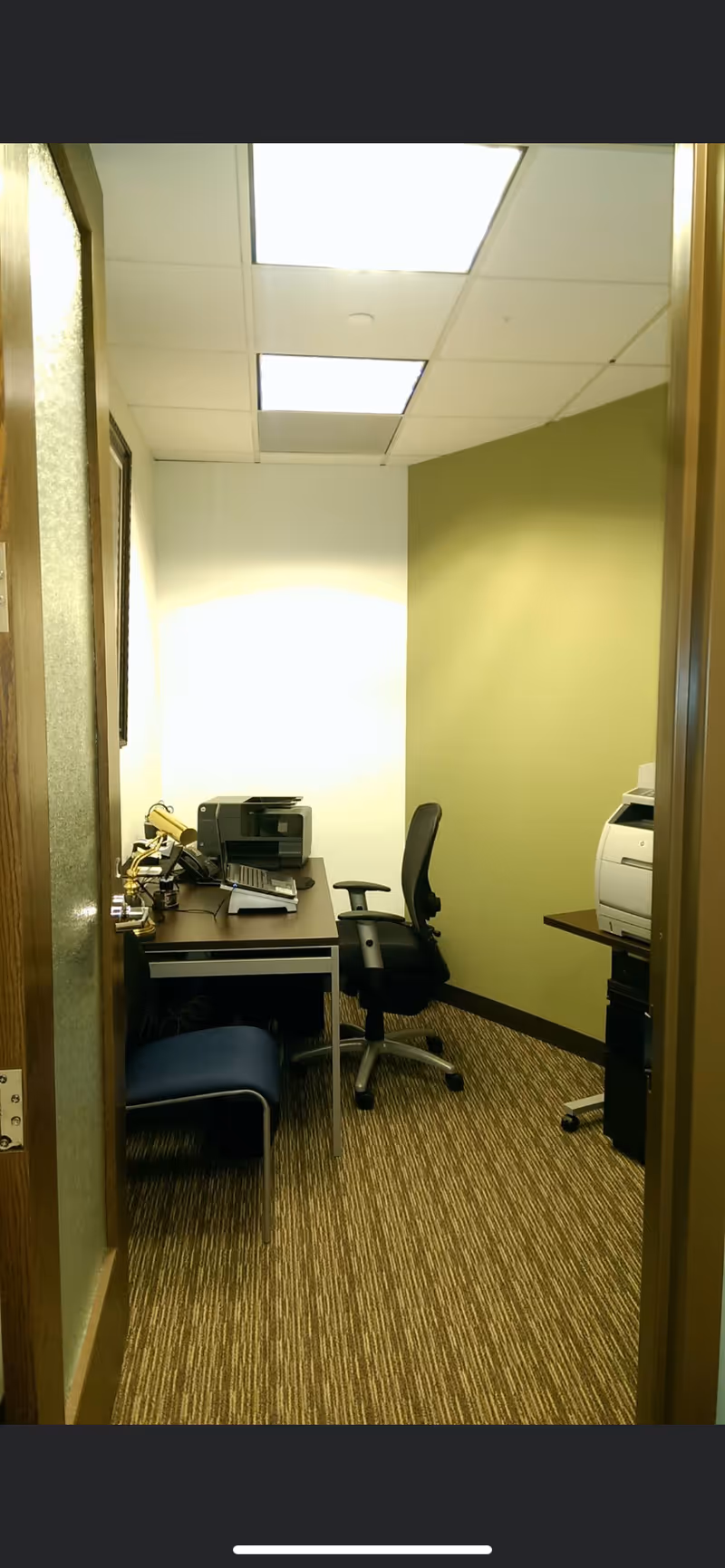 Small office with desk, computer, chair, printer, and filing equipment in a narrow room.
