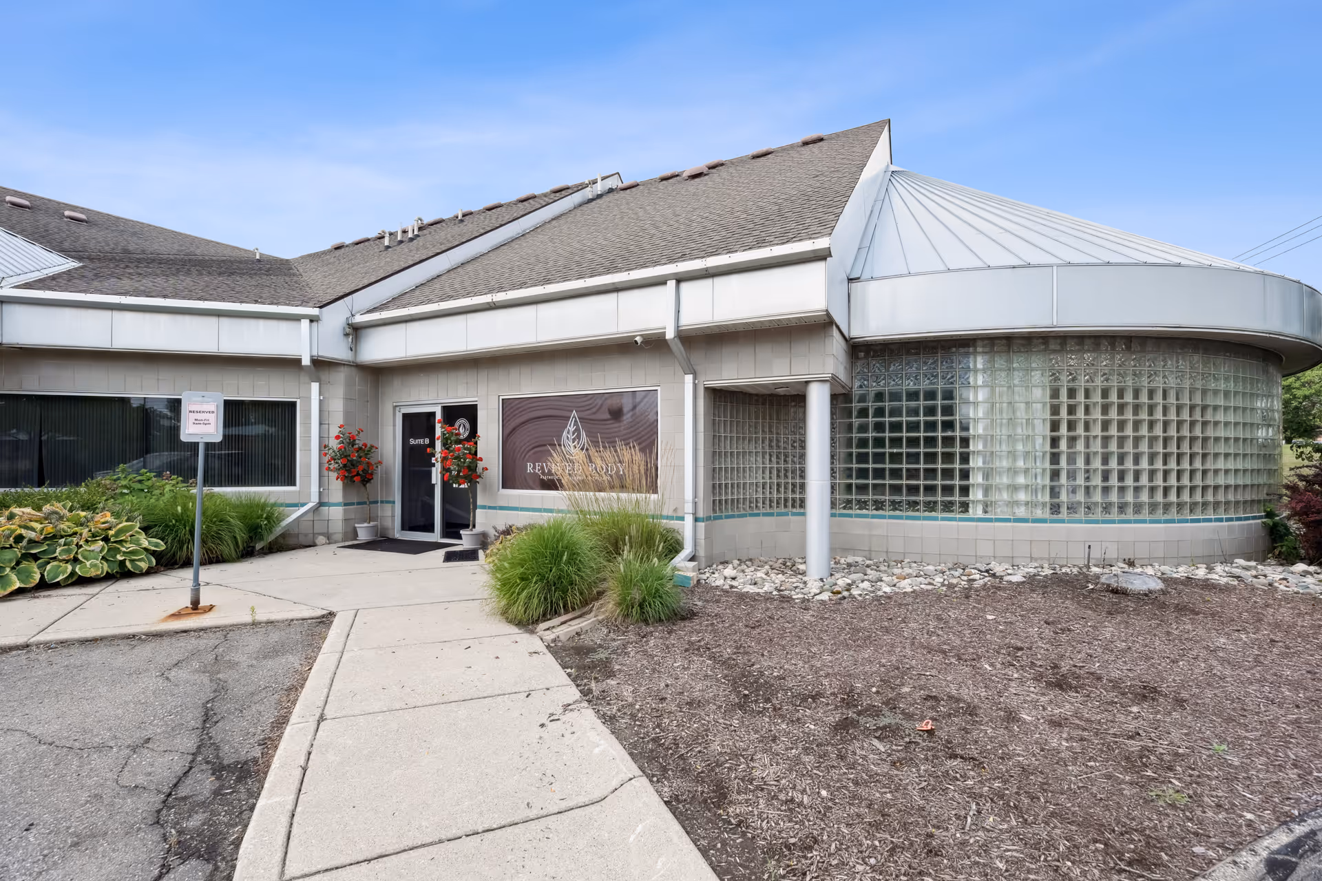 Exterior view of Revived Body clinic with curved glass entrance and landscaped surroundings.