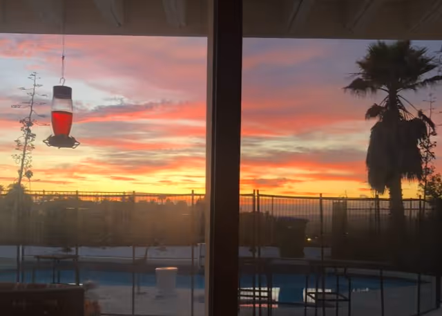 Sunset view over a pool area seen through sliding glass doors.
