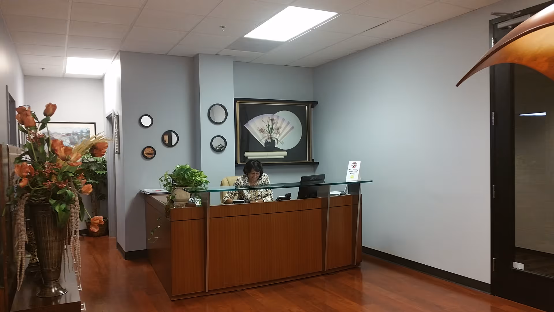 Reception desk with glass top, a receptionist working in a softly lit wood-floored lobby.
