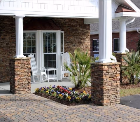 Exterior view of Woodbury Wellness Center with stone columns, rocking chairs, and flower bed.